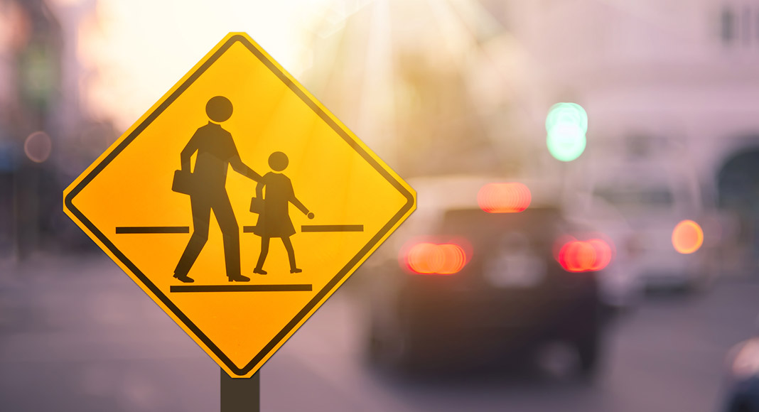School zone warning sign on blur traffic road with colorful bokeh light abstract background.